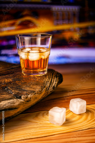 A glass of alcoholic beverage on a wooden table against the background of the night city. Whiskey cocktail with ice