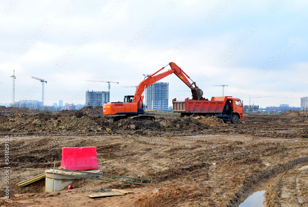 Excavator load the sand to the heavy dump truck on construction site. Excavators and dozers digs the ground for the foundation and construction of a new building. Apartment renovation program Excavator load the sand to the heavy dump truck on construction site. Excavators and dozers digs the ground for the foundation and construction of a new building. Apartment renovation program