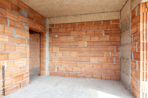 Unfinished room interior of building under construction. Brick red walls. New home. © dechevm