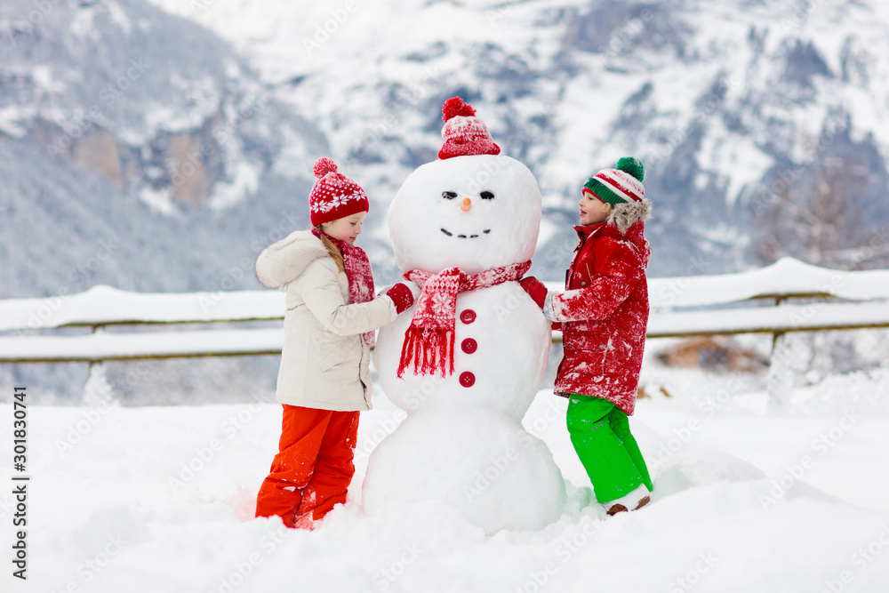 Child building snowman. Kids build snow man.