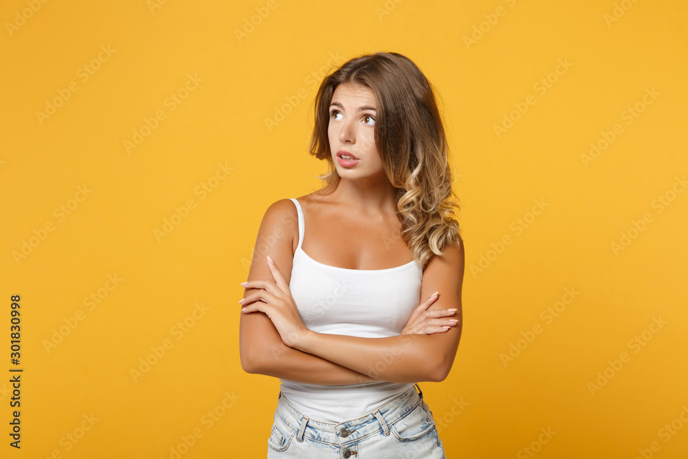 Pensive confused young woman in light casual clothes posing isolated on yellow orange background studio portrait . People lifestyle concept. Mock up copy space. Holding hands crossed looking aside up. Pensive confused young woman in light casual clothes posing isolated on yellow orange background studio portrait . People lifestyle concept. Mock up copy space. Holding hands crossed looking aside up.