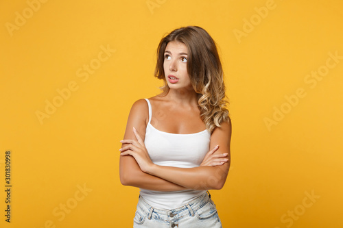 Pensive confused young woman in light casual clothes posing isolated on yellow orange background studio portrait . People lifestyle concept. Mock up copy space. Holding hands crossed looking aside up.