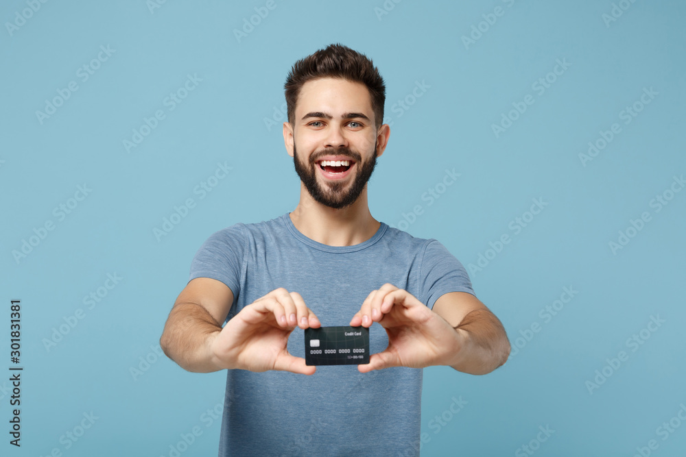 Young cheerful laughing attractive man in casual clothes posing isolated on blue wall background studio portrait. People sincere emotions lifestyle concept. Mock up copy space. Hold credit bank card. Young cheerful laughing attractive man in casual clothes posing isolated on blue wall background studio portrait. People sincere emotions lifestyle concept. Mock up copy space. Hold credit bank card.
