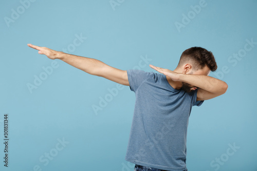 Young man in casual clothes posing isolated on blue wall background, studio portrait. People sincere emotions lifestyle concept. Mock up copy space. Showing dab dance gesture.
