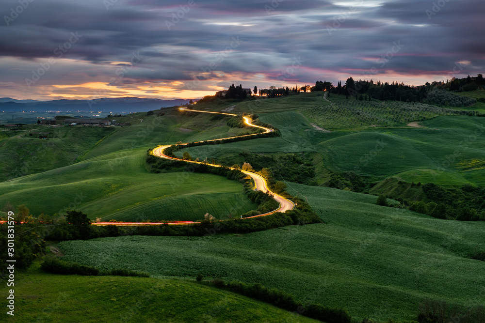 Fototapeta premium Kręta droga, światła samochodów, zachód słońca w tle, Toskania, Włochy