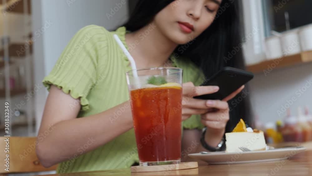 Young Asian woman using smartphone drinking coffee in cafe chatting with friends. Girl using cellphone in coffee shop. Young Asian woman using smartphone drinking coffee in cafe chatting with friends. Girl using cellphone in coffee shop.