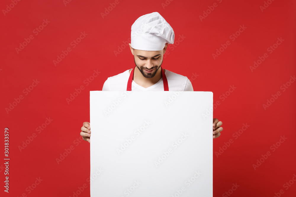 Young bearded male chef cook or baker man in toque chefs hat isolated on red background. Cooking food concept. Mock up copy space. Holding big white empty blank billboard with place for text or image. Young bearded male chef cook or baker man in toque chefs hat isolated on red background. Cooking food concept. Mock up copy space. Holding big white empty blank billboard with place for text or image.