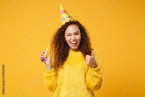 Canvas Print Cheerful young african american girl in fur sweater, birthday hat posing isolated on yellow orange background