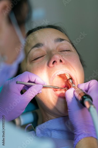 Dentist and patient in dentist office. Close-up of dental drill use for patient teeth in dentistry office in a dental treatment procedure. Woman having teeth examined at dentists. vertical photo