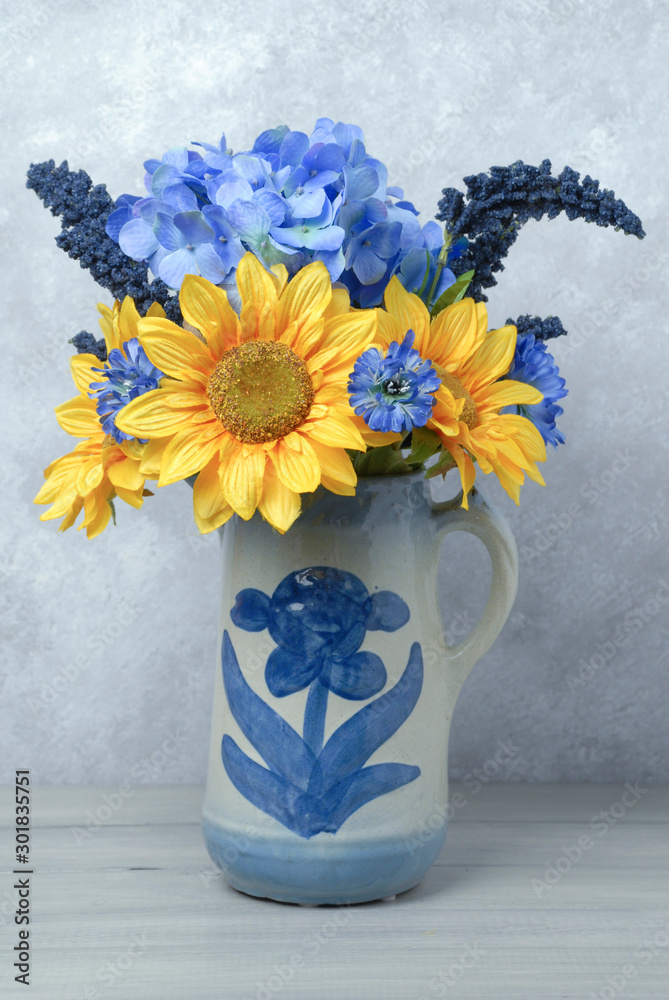Bouquet of sunflowers and blue flowers in an old antique vase on a grey ...