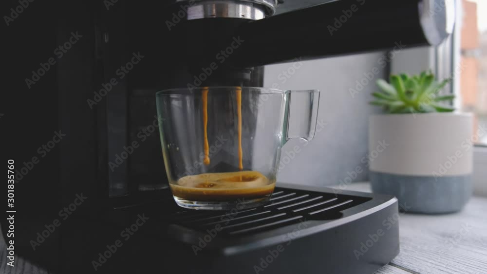 Coffee machine making espresso in glass transparent coffee cup. Hot espresso running into cup.