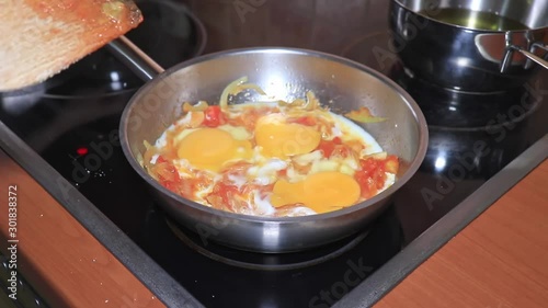 The chef cooking an omelet, scrumbled eggs in a pan with a chopped tomatoes and onion, cooking omelet with vegetables at home close up photo