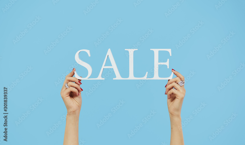 Fototapeta premium Female hands hold a sign with the inscription sale on a blue isolated background. Christmas and holiday sales concept
