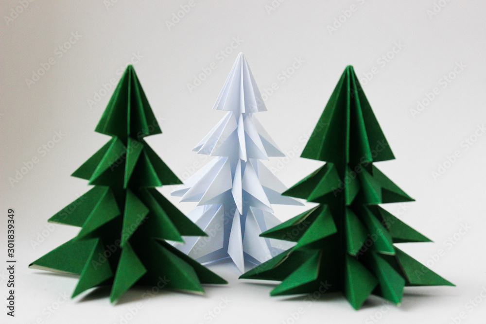 Two origami green christmas tree and white one on white background. Focus on a white tree behind green Two origami green christmas tree and white one on white background. Focus on a white tree behind green