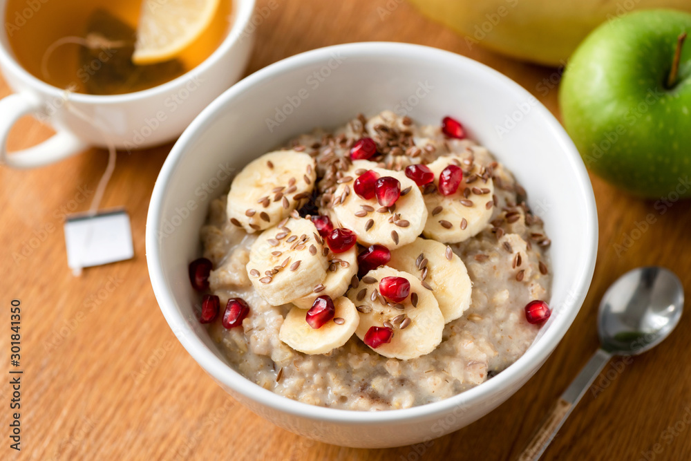 Porridge oats or oatmeal in bowl with banana slice, pomegranate seeds and flax seeds on a wooden table background. Selective focus. Healthy breakfast, healthy lifestyle, dieting concept Porridge oats or oatmeal in bowl with banana slice, pomegranate seeds and flax seeds on a wooden table background. Selective focus. Healthy breakfast, healthy lifestyle, dieting concept