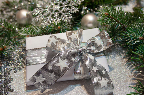 Bożonarodzeniowe tło z biało-srebrnym prezentem, srebrnymi ozdobami i gałązkami świerku