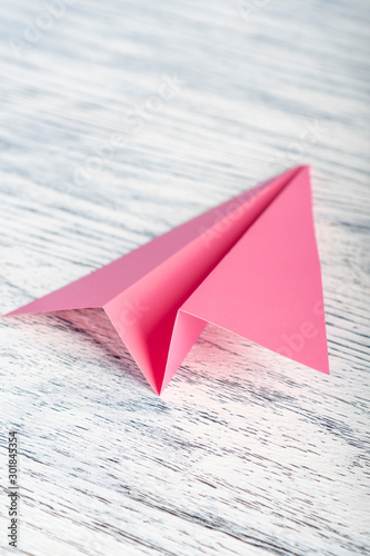 Pink paper airplane on a wooden white background
