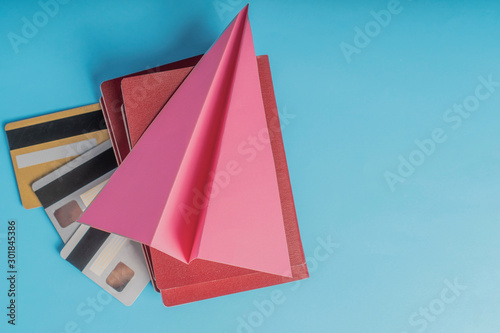 Red passports with credit cards lie on a blue background under a pink paper airplane