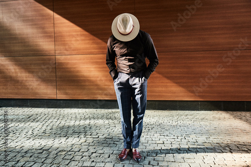 A man in a hat stylish standing on a street on block pavement at wooden wall on  photo