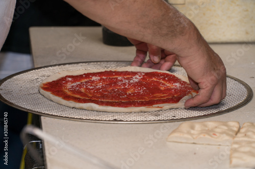 A delicious small pizza pie being prepared in New York City style pizzeria by old school italian immigrant hard working for customer order delivery for meal