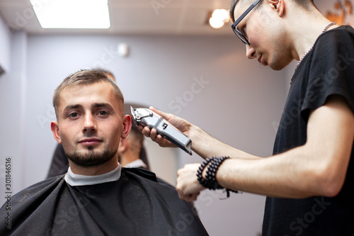 young guy makes a short haircut in a barbershop with a trimmer, close-up