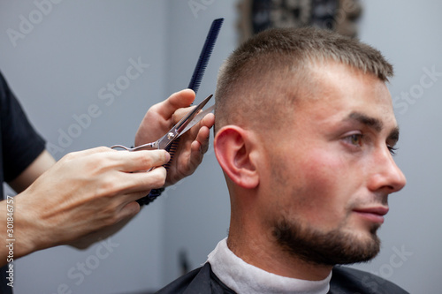 handsome guy get a haircut at the hairdresser, Kazakh hairdresser cuts manually with scissors and a comb, short haircut close-up