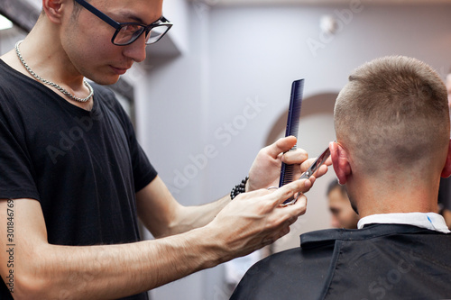 guy get a haircut in a barbershop, a young Kazakh barber cuts manually with scissors and a comb, the master makes a short haircut at the hairdresser