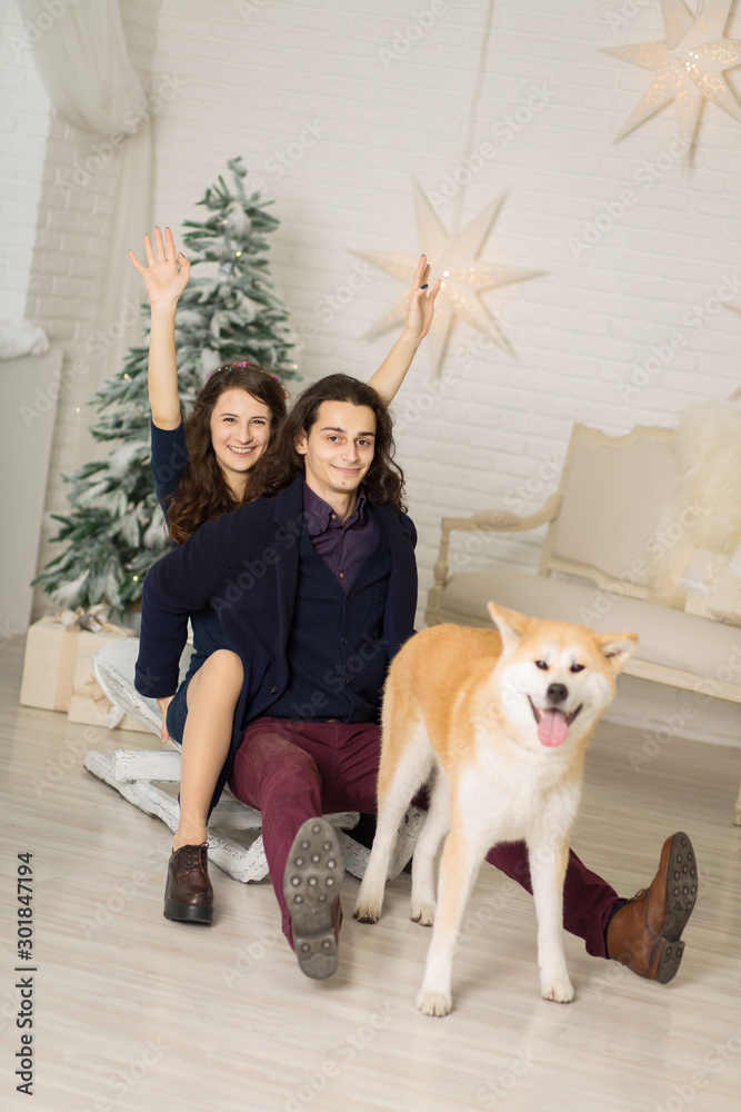 cheerful young couple on a sled with a dog in Christmas decorations