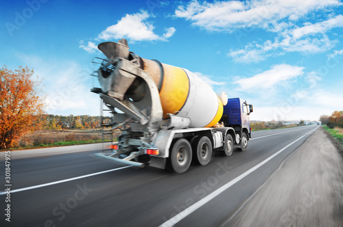 Concrete mixer truck driving fast on the countryside road against sky