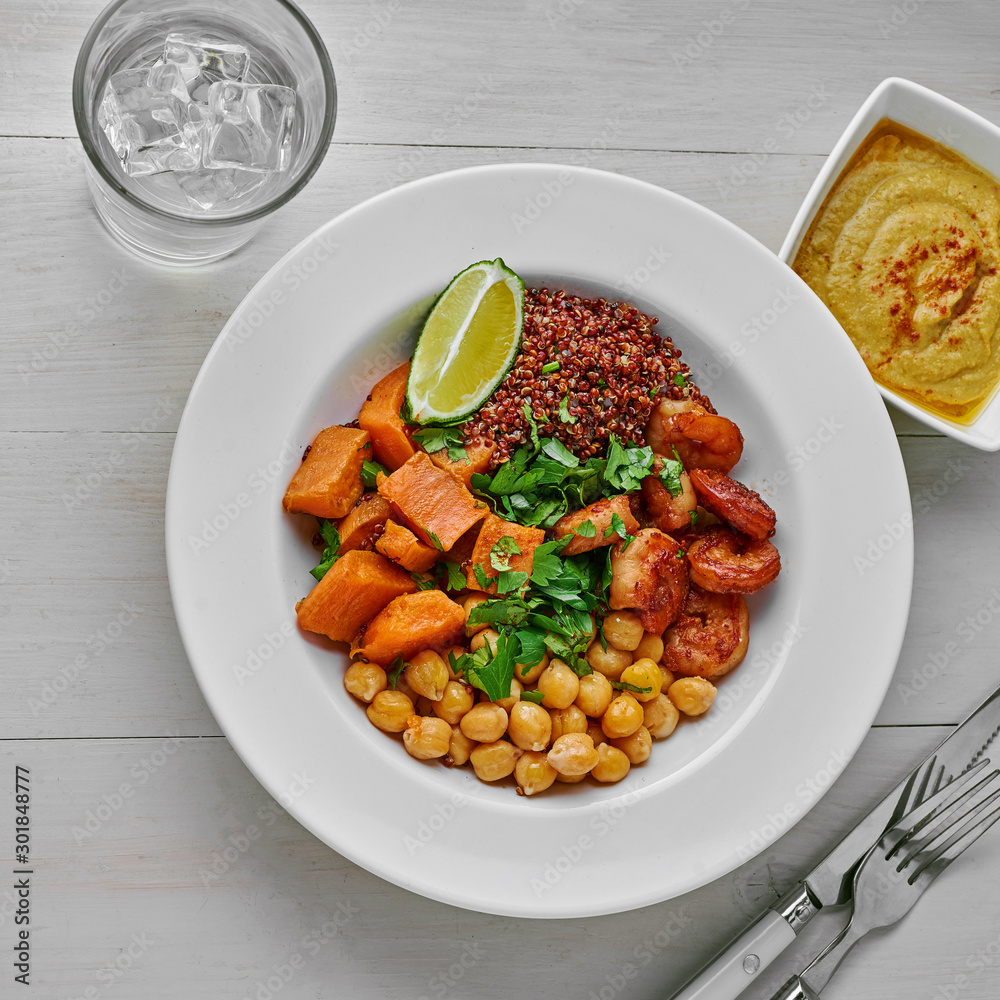 Healthy lunch bowl made of shrimp and vegetables with humus, parsley and lime on a white rustic table with a glass of cool water. Top view, directly above.