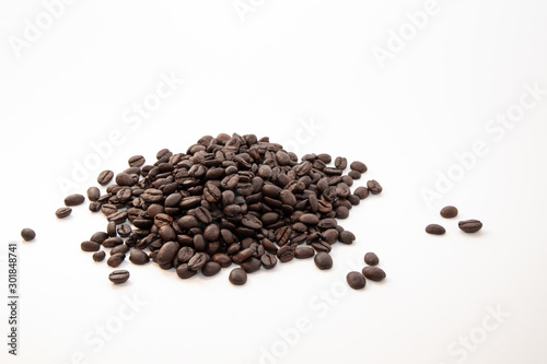 Dark roasted coffee beans on a pile on a white surface