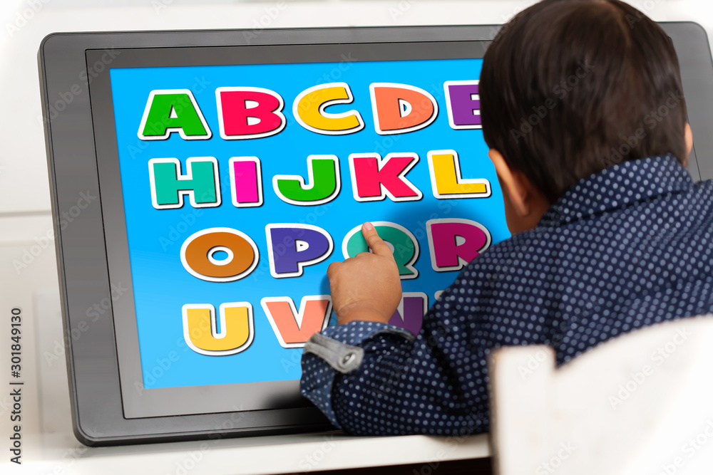 Naklejka premium A young boy using a touchscreen to play a learning app.