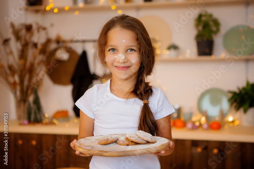 baby girl brunette is preparing gingerbread in Christmas kitchen. little girl smiling in Christmas kitchen covered in flour