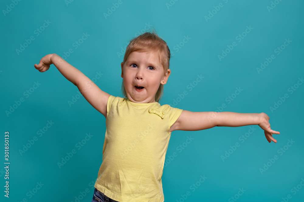 Close-up studio shot of a beautiful little girl. Little blonde girl in a yellow T-shirt on a blue background. The emotions of a child. Close-up studio shot of a beautiful little girl. Little blonde girl in a yellow T-shirt on a blue background. The emotions of a child.