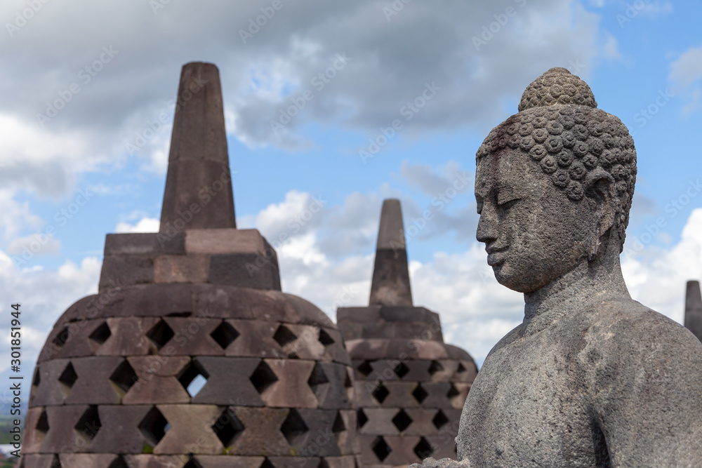 Obraz premium A Buddah in his stupa of Borobodur overlooking the surrounding land and watching over the volcanoes. Some of them are opened during dry season. A stunning monument in Central Java, Indonesia.
