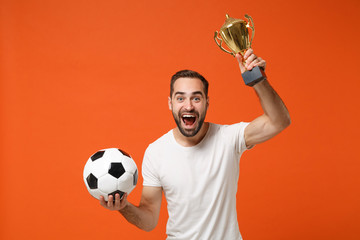 Excited young man in casual white t-shirt posing isolated on orange wall background studio portrait. People sincere emotions lifestyle concept. Mock up copy space. Holding soccer ball, football cup.