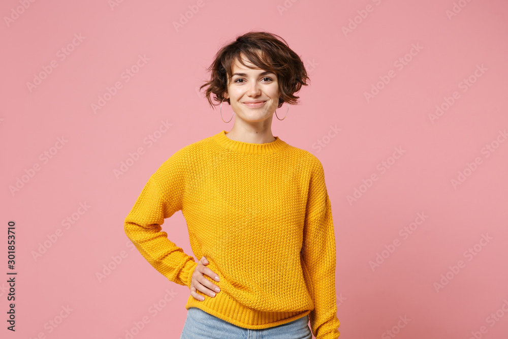 Smiling young brunette woman girl in yellow sweater posing isolated on pastel pink wall background, studio portrait. People sincere emotions lifestyle concept. Mock up copy space. Looking camera. - obrazy, fototapety, plakaty 