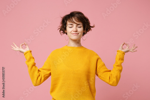 Young brunette woman girl in yellow sweater posing isolated on pastel pink background. People lifestyle concept. Mock up copy space. Hold hands in yoga gesture relaxing meditating keeping eyes closed. photo