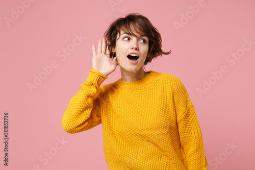 фотографія Curious young brunette woman girl in yellow sweater posing isolated on pastel pink wall background, studio portrait