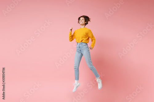 Funny young brunette woman girl in yellow sweater posing isolated on pastel pink background in studio. People lifestyle concept. Mock up copy space. Having fun fooling around, looking aside, jumping.