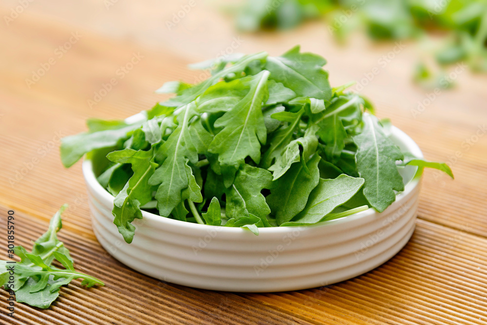 Fresh green rocket salad in white round plate. Healthy salad isolated on wooden table. Copy space. Fresh green rocket salad in white round plate. Healthy salad isolated on wooden table. Copy space.