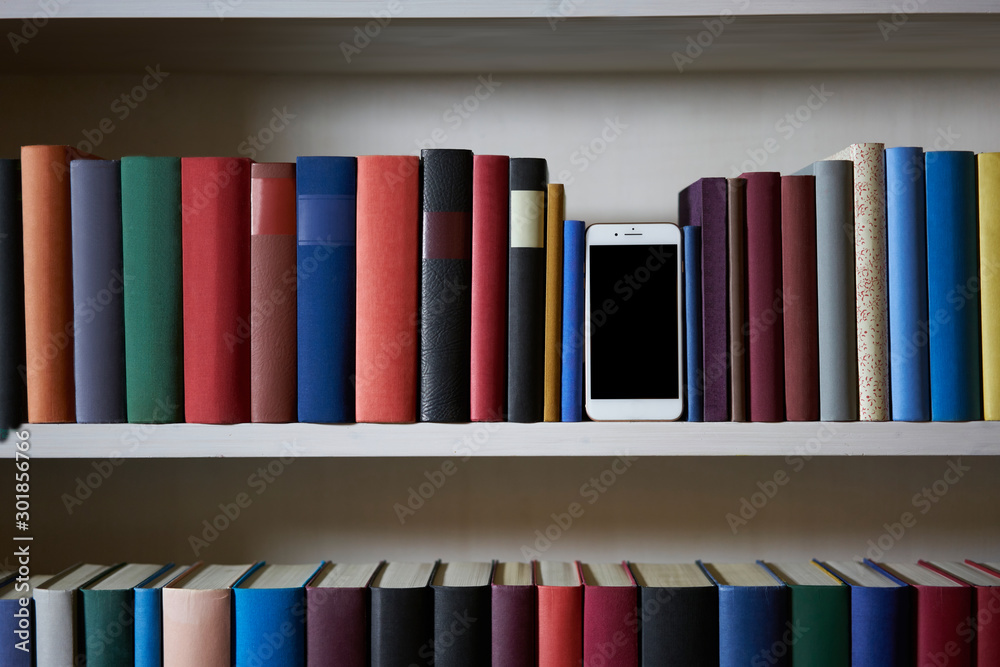 Fototapeta premium Mobile phone between accurately sorted bookshelf