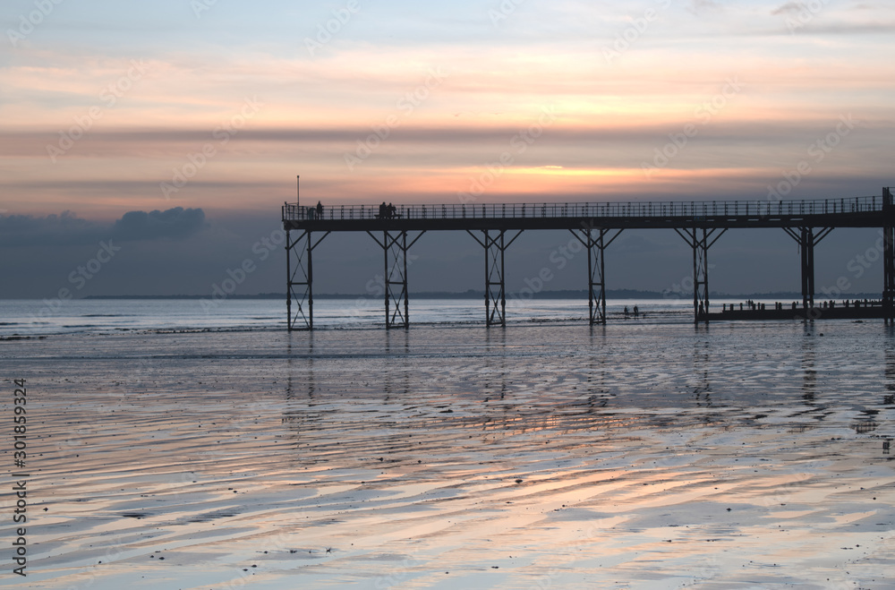 Historic old Pier in Bognor Regis West Sussex with a beautiful sunset behind and reflections on the sand at low tide.