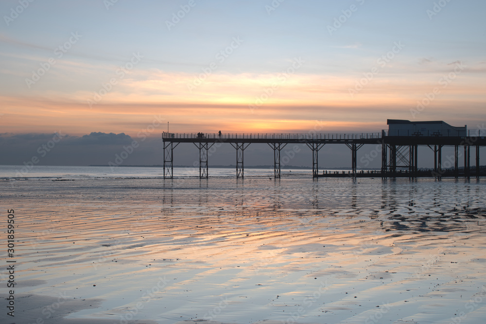 Pier in Bognor Regis West Sussex with a beautiful sunset behind and reflections on the sand at low tide.