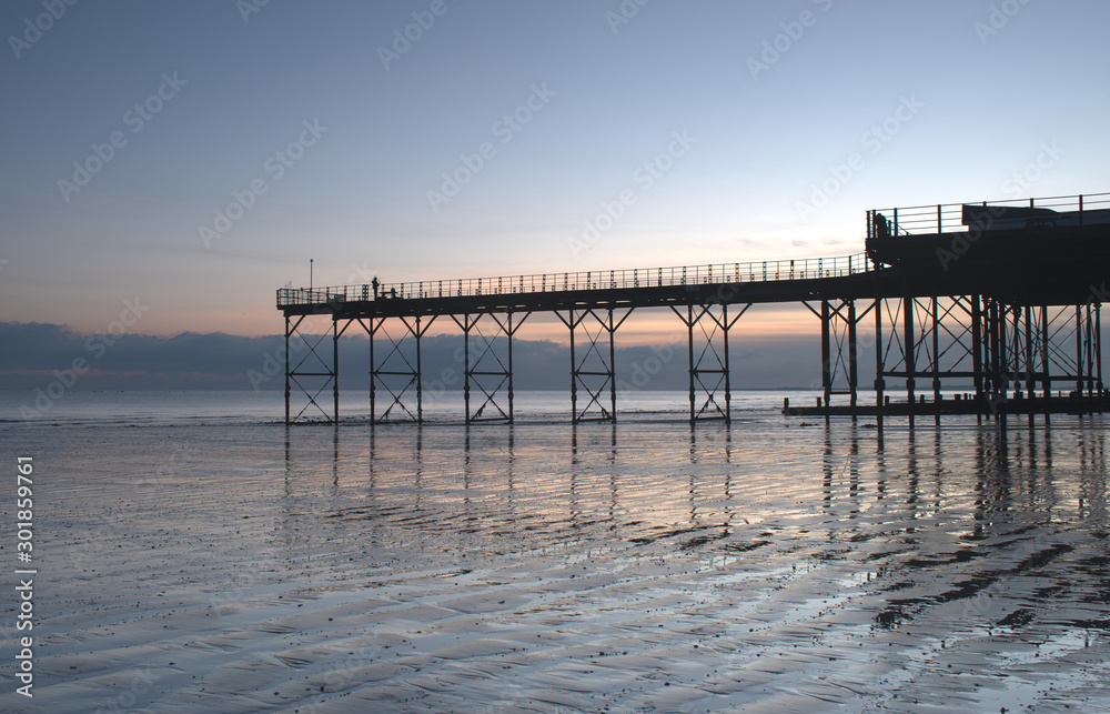 View of the Pier in Bognor Regis West Sussex with a beautiful sunset behind and reflections on the sand at low tide.