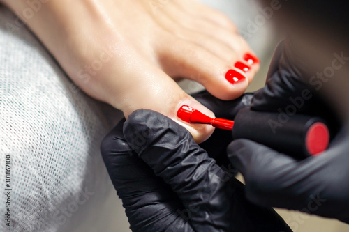 Woman receiving nail polishing with red nail polish on fingers of feet by professional podiatrist close up.