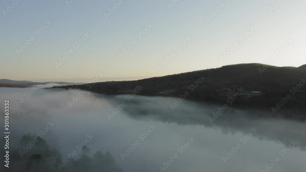 Curving around a bank of fog with a farmhouse on a hillside in the distance AERIaL SUNRISE Curving around a bank of fog with a farmhouse on a hillside in the distance AERIaL SUNRISE
