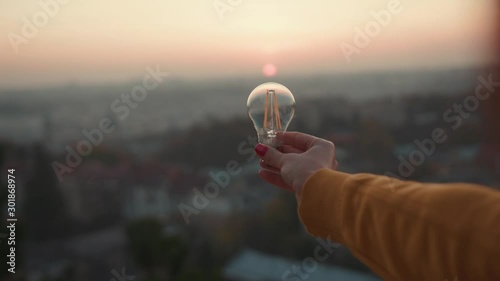 Close up hands woman holds a house light bulb at sunset renewable energy nature electricity innovation green invention responsibility environment adult power protect lamp slow motion