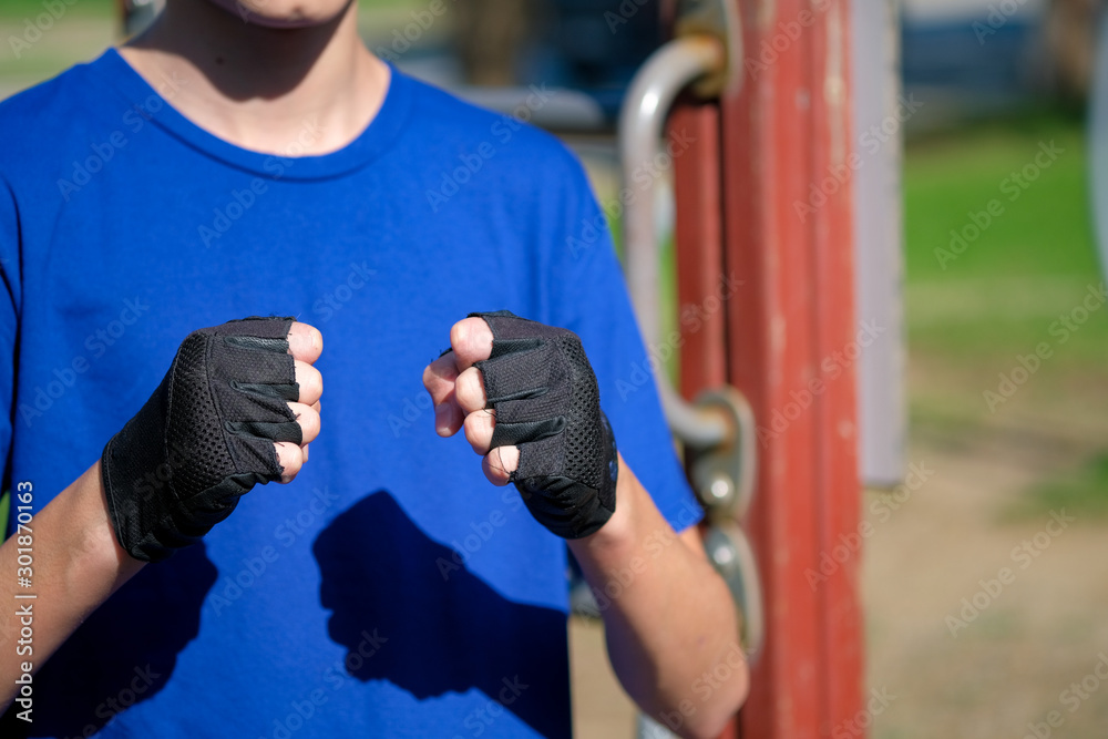 Obraz premium Teenager wears suede leather grips for outdoor workout on blurred background. Gesture of a boy ready for battle fight. Healthy active lifestyle, muscle strengthening power loads. Outdoor sports ground