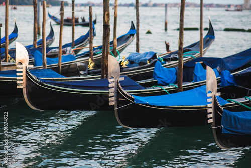 Traditional venetian gondolas by the waterfront. Several boats for travelers and tourists are covered with covers at the pier. © Evgenii Starkov